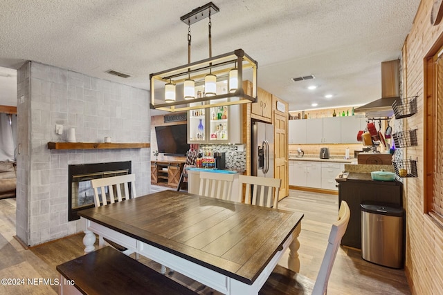 dining room featuring a textured ceiling, light wood-type flooring, and a large fireplace