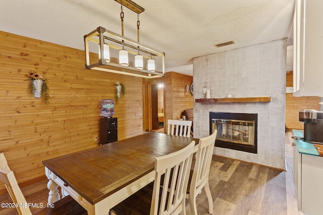 dining room with wood walls, dark wood-type flooring, a fireplace, and a textured ceiling