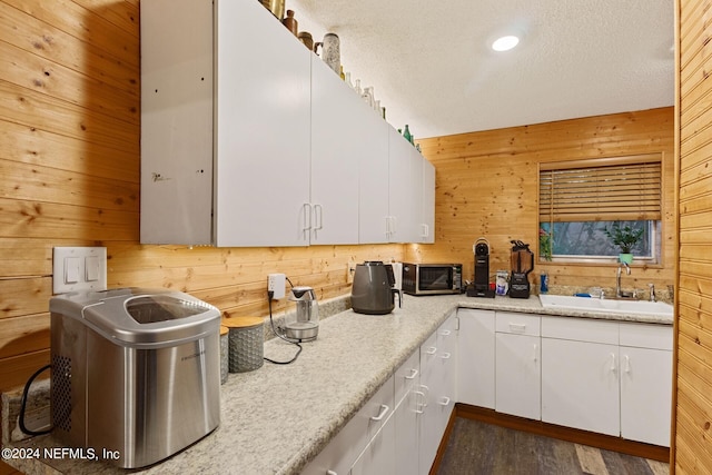 kitchen featuring wood walls, sink, a textured ceiling, white cabinetry, and hardwood / wood-style floors