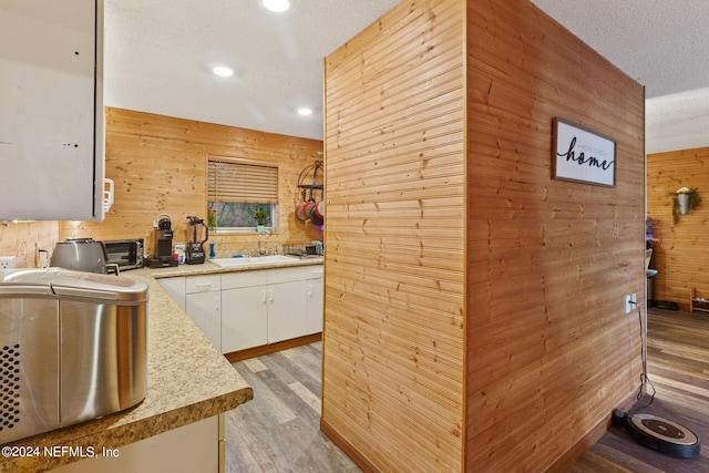 kitchen featuring white cabinets, a textured ceiling, light wood-type flooring, and wooden walls