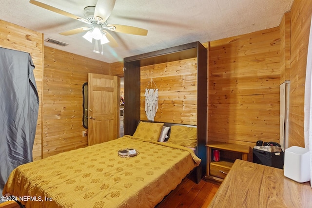 bedroom featuring wood walls, dark wood-type flooring, ceiling fan, and a textured ceiling