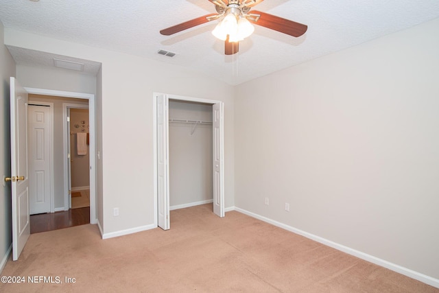 unfurnished bedroom with a textured ceiling, light colored carpet, ceiling fan, and a closet