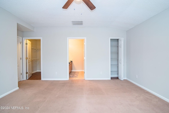 unfurnished bedroom with connected bathroom, ceiling fan, vaulted ceiling, a walk in closet, and light colored carpet