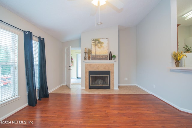 unfurnished living room featuring a tile fireplace, vaulted ceiling, wood-type flooring, ceiling fan, and a textured ceiling