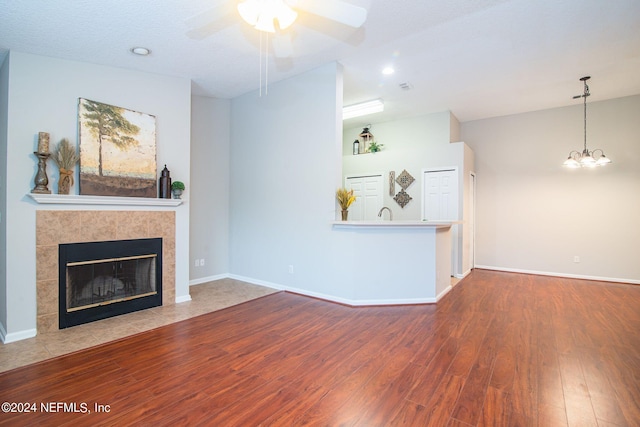 living room with ceiling fan with notable chandelier, a tile fireplace, hardwood / wood-style flooring, and a textured ceiling