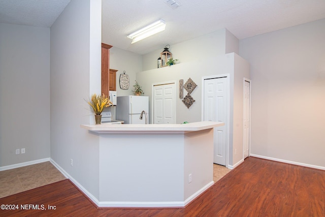 kitchen with white appliances, light hardwood / wood-style flooring, kitchen peninsula, and a textured ceiling