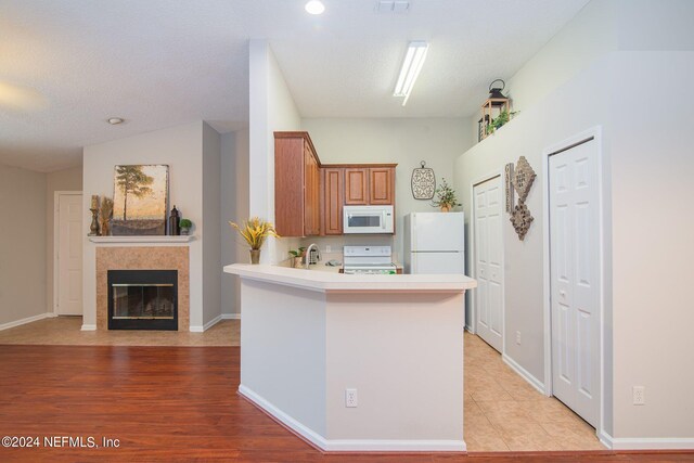 kitchen with a textured ceiling, vaulted ceiling, white appliances, a fireplace, and light hardwood / wood-style floors