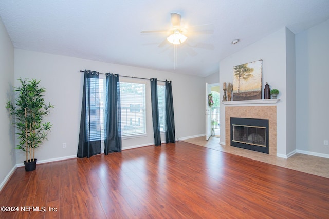 unfurnished living room with lofted ceiling, ceiling fan, a tiled fireplace, and wood-type flooring