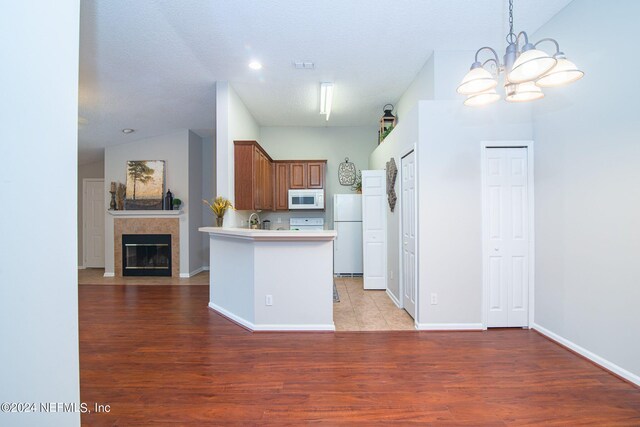 kitchen featuring a textured ceiling, white appliances, light hardwood / wood-style floors, a chandelier, and lofted ceiling