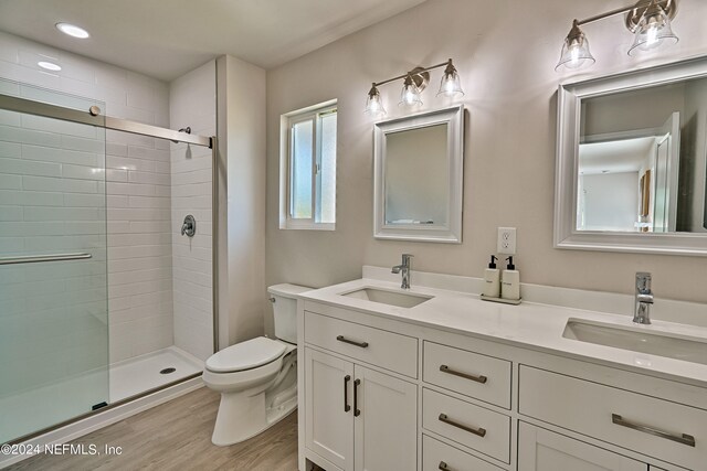 bathroom featuring hardwood / wood-style floors, a shower with shower door, toilet, and double sink vanity