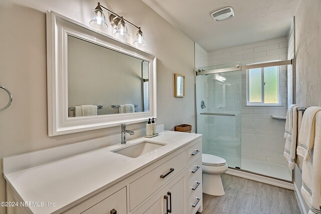 bathroom featuring hardwood / wood-style flooring, a shower with door, toilet, and vanity with extensive cabinet space