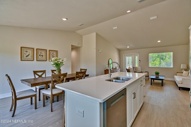 kitchen with light wood-type flooring, white cabinetry, sink, vaulted ceiling, and an island with sink