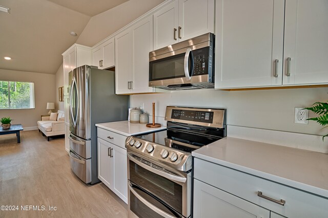 kitchen with light hardwood / wood-style floors, stainless steel appliances, white cabinetry, and lofted ceiling