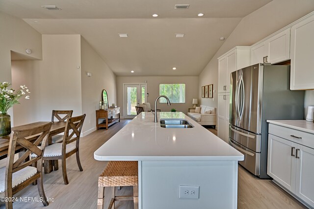 kitchen with light hardwood / wood-style flooring, vaulted ceiling, an island with sink, white cabinets, and sink