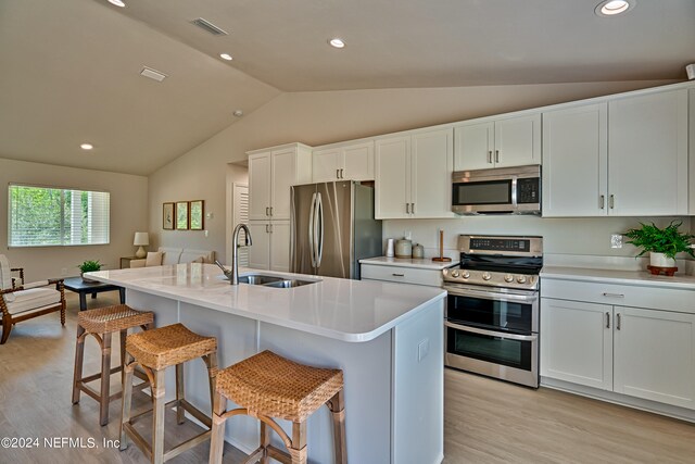 kitchen with white cabinets, stainless steel appliances, sink, light hardwood / wood-style floors, and lofted ceiling