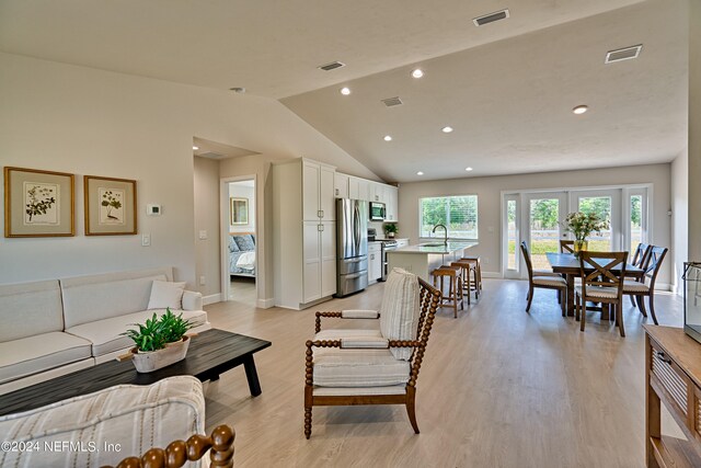 living room with lofted ceiling, sink, light wood-type flooring, and french doors