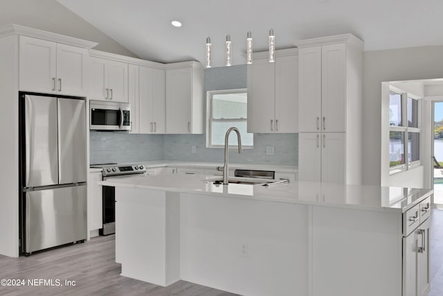 kitchen with lofted ceiling, appliances with stainless steel finishes, white cabinets, and an island with sink