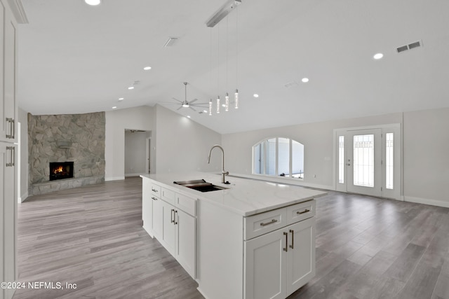 kitchen featuring a stone fireplace, vaulted ceiling, light hardwood / wood-style floors, an island with sink, and sink