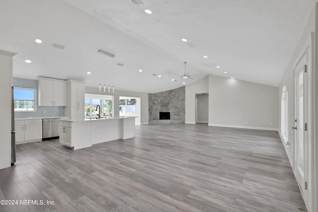 unfurnished living room with ceiling fan, a stone fireplace, a textured ceiling, lofted ceiling, and light hardwood / wood-style flooring