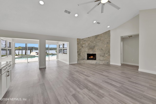 unfurnished living room with light hardwood / wood-style flooring, high vaulted ceiling, ceiling fan, and a stone fireplace