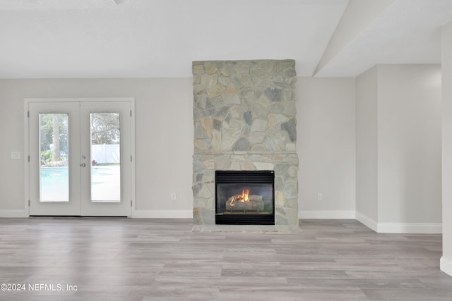 unfurnished living room with vaulted ceiling, french doors, light wood-type flooring, and a fireplace