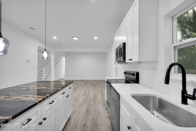 kitchen featuring dark stone countertops, stainless steel appliances, pendant lighting, and light hardwood / wood-style floors