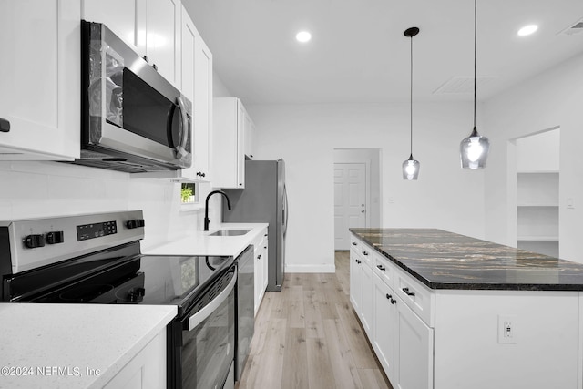 kitchen featuring hanging light fixtures, white cabinets, light wood-type flooring, appliances with stainless steel finishes, and dark stone countertops