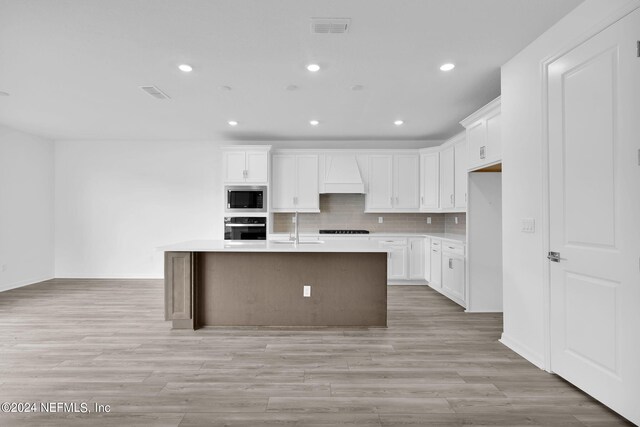 kitchen with white cabinets, appliances with stainless steel finishes, a center island with sink, and custom range hood