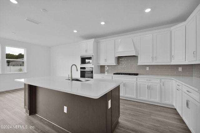 kitchen with backsplash, custom range hood, sink, black appliances, and a center island with sink