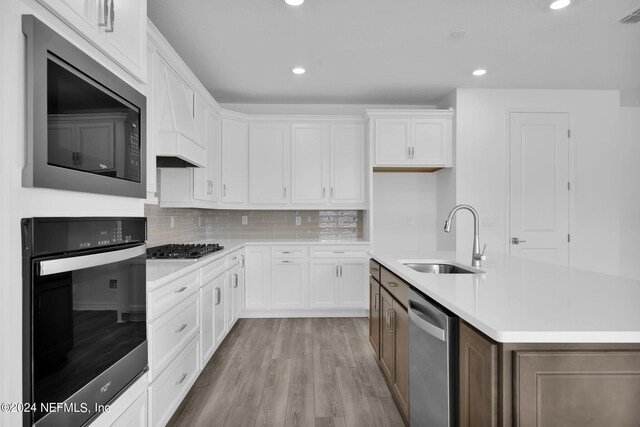 kitchen featuring light hardwood / wood-style flooring, appliances with stainless steel finishes, a kitchen island with sink, sink, and white cabinets