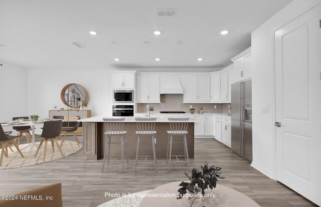 kitchen with built in microwave, black oven, custom range hood, an island with sink, and stainless steel fridge with ice dispenser