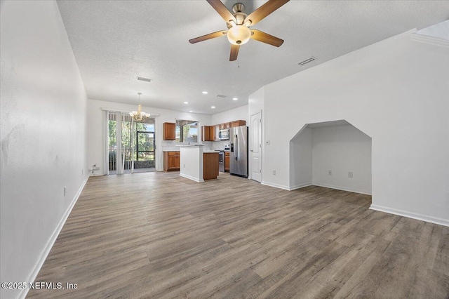 unfurnished living room featuring ceiling fan with notable chandelier, wood-type flooring, and a textured ceiling