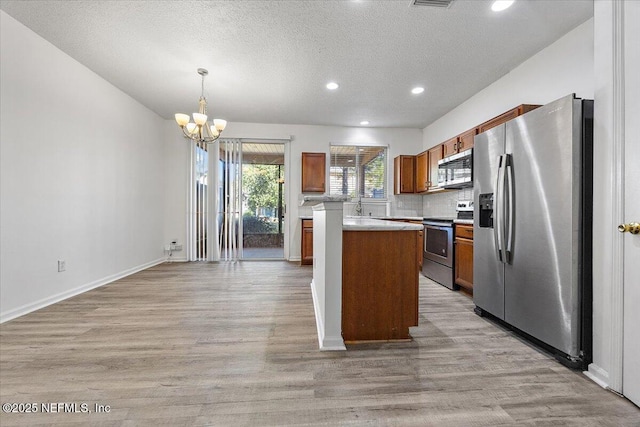 kitchen with hanging light fixtures, appliances with stainless steel finishes, a center island, and light hardwood / wood-style flooring