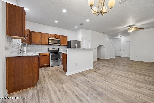 kitchen with appliances with stainless steel finishes, pendant lighting, sink, a center island, and light hardwood / wood-style flooring