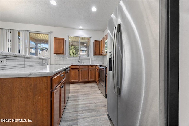 kitchen featuring sink, a textured ceiling, light hardwood / wood-style flooring, appliances with stainless steel finishes, and decorative backsplash