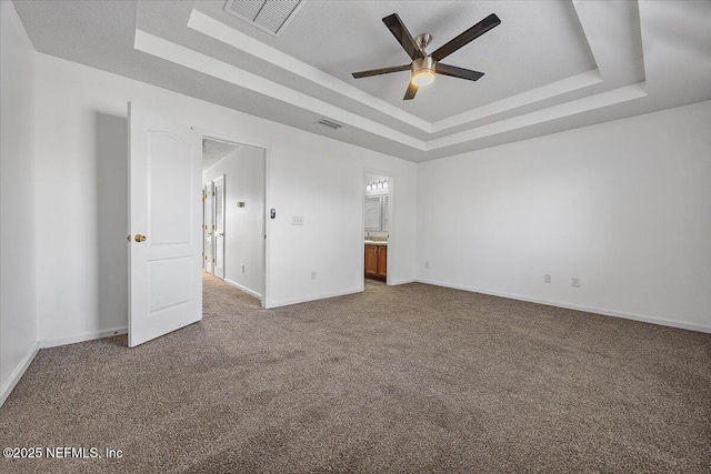 unfurnished bedroom with ensuite bathroom, a raised ceiling, and carpet