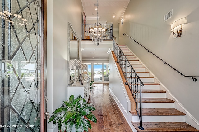 staircase with a chandelier, crown molding, and wood-type flooring