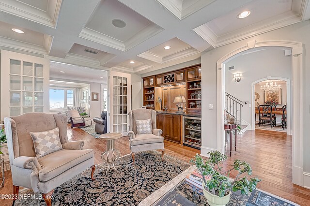 sitting room featuring light hardwood / wood-style flooring, beverage cooler, beam ceiling, coffered ceiling, and ornamental molding