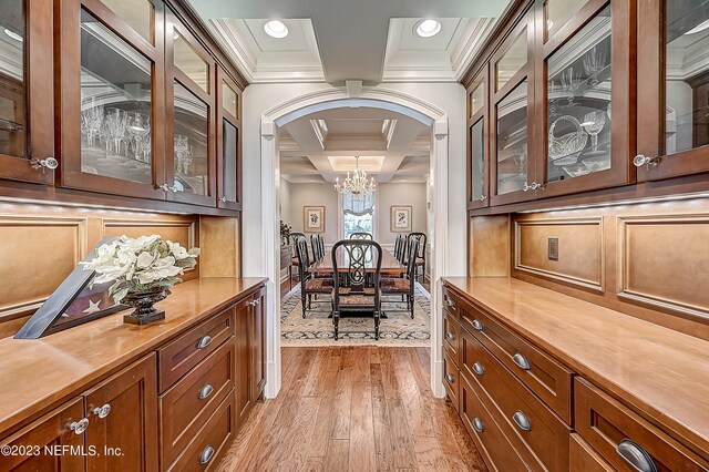 interior space featuring light hardwood / wood-style flooring, ornamental molding, an inviting chandelier, beam ceiling, and coffered ceiling