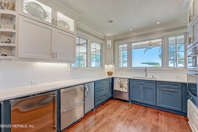 kitchen with white cabinets, sink, blue cabinetry, stainless steel appliances, and light hardwood / wood-style flooring