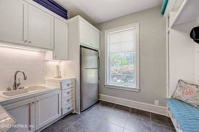 kitchen with stainless steel refrigerator, white cabinetry, tile flooring, sink, and tasteful backsplash