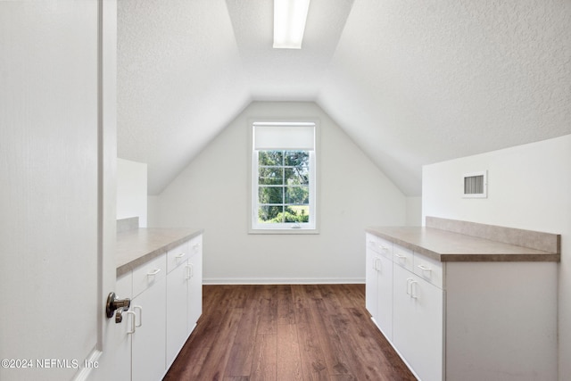 bonus room with lofted ceiling, dark wood-type flooring, and a textured ceiling