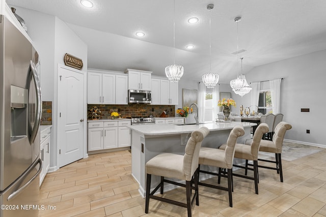 kitchen with white cabinets, backsplash, decorative light fixtures, stainless steel appliances, and an island with sink