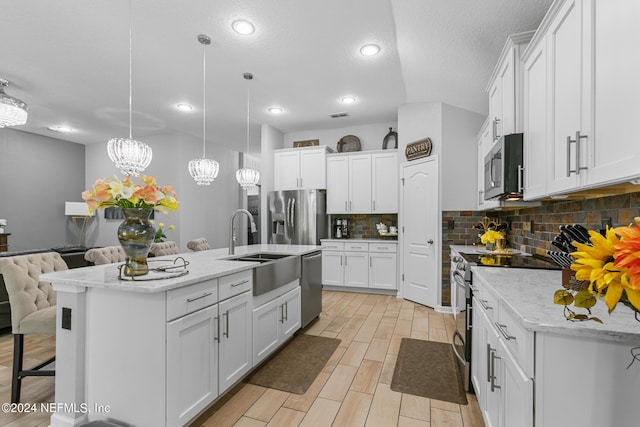 kitchen with backsplash, white cabinetry, decorative light fixtures, stainless steel appliances, and a center island with sink