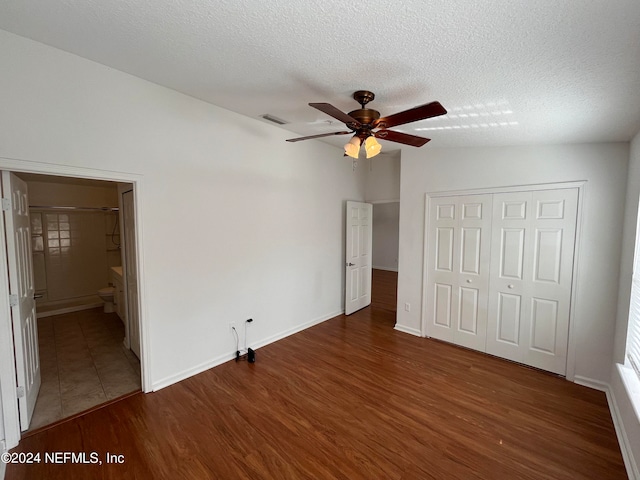 unfurnished bedroom featuring ensuite bathroom, a textured ceiling, a closet, ceiling fan, and dark hardwood / wood-style floors