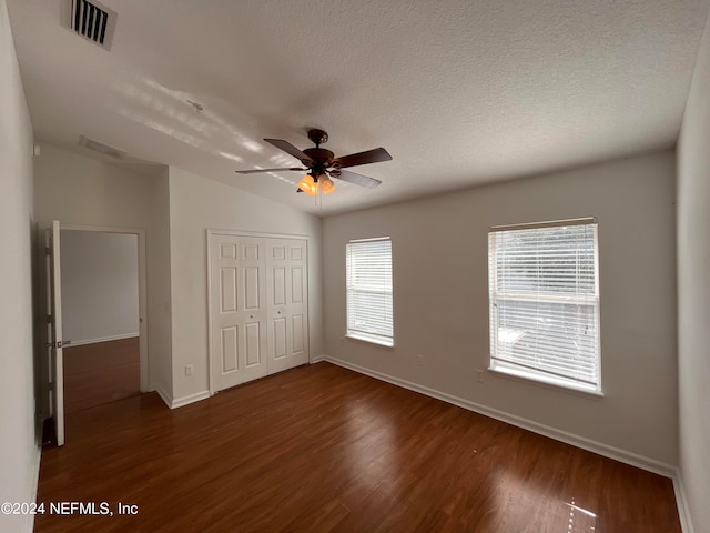 unfurnished bedroom with a closet, vaulted ceiling, dark hardwood / wood-style flooring, a textured ceiling, and ceiling fan