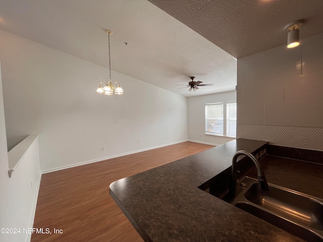 kitchen with a textured ceiling, dark wood-type flooring, ceiling fan with notable chandelier, pendant lighting, and sink