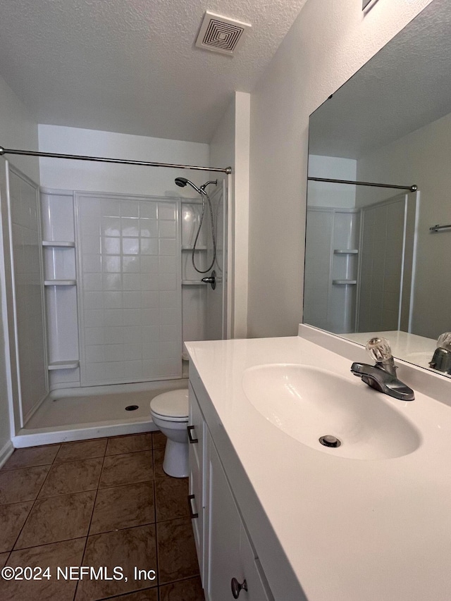 bathroom featuring a textured ceiling, toilet, walk in shower, vanity, and tile patterned flooring