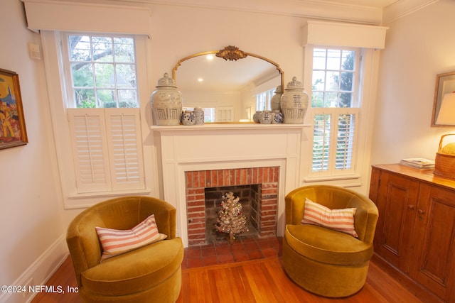 sitting room featuring wood-type flooring, a wealth of natural light, crown molding, and a brick fireplace