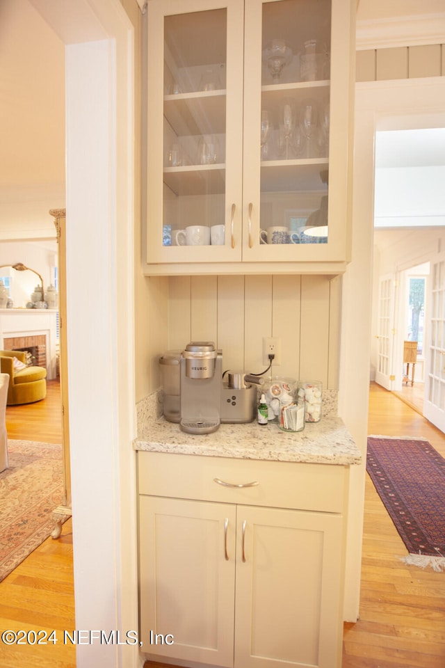 bar featuring light hardwood / wood-style flooring, a brick fireplace, and light stone countertops